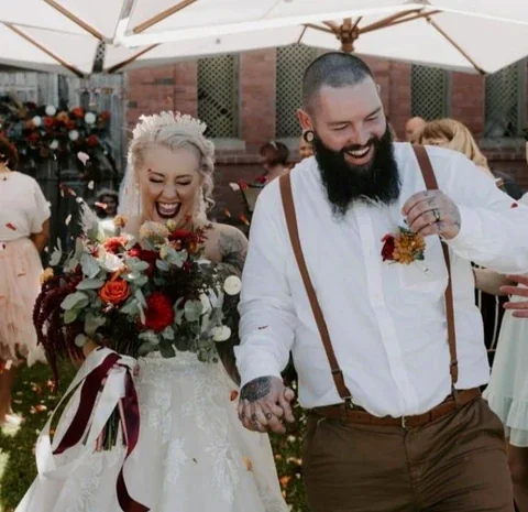 A newly married couple walk hand in hand carrying a bouquet and matching boutonniere.