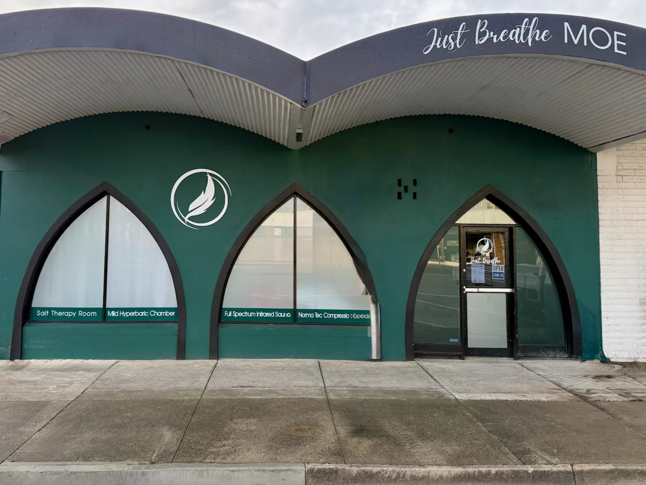 The green Just Breathe shopfront in Moe, with three pointed-arch windows beneath the Just Breathe Moe sign.