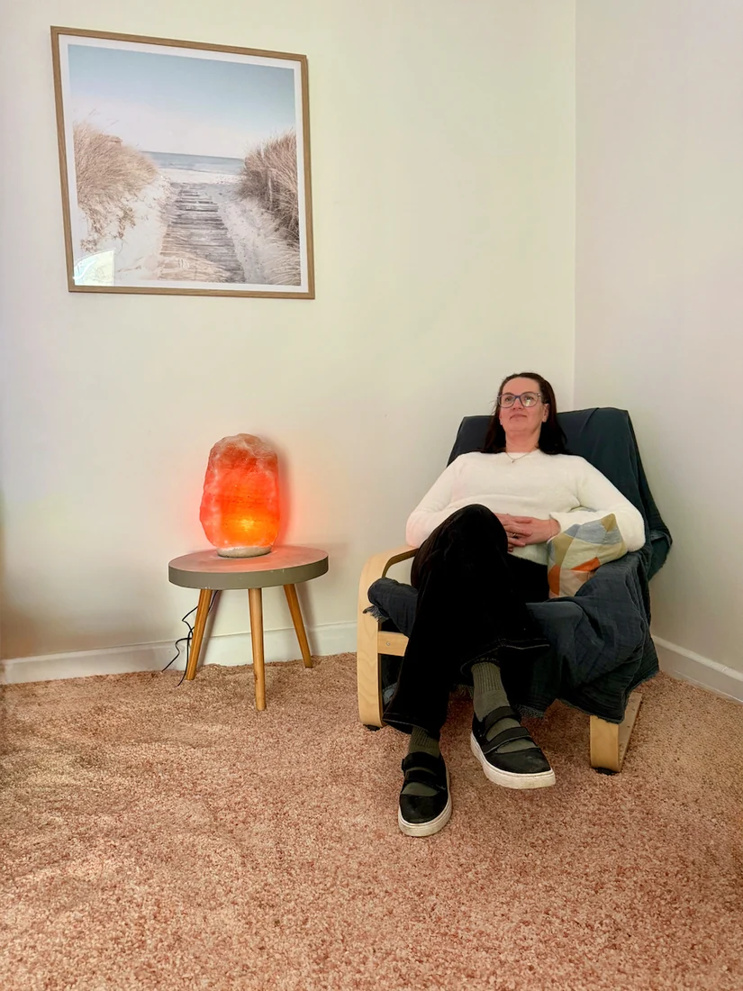 Wendy Stanway reclines in a dark chair beside a glowing orange salt lamp.