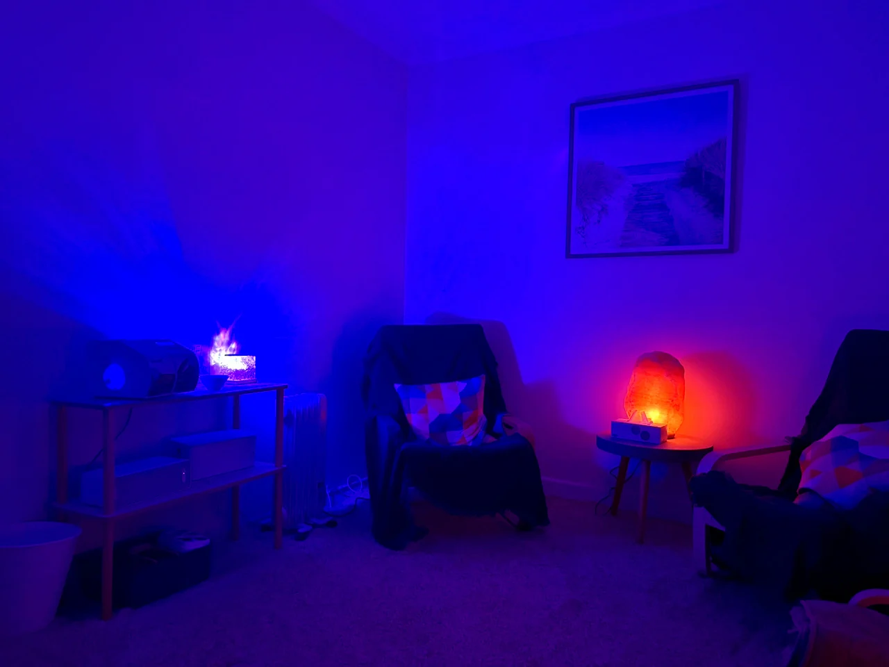 Two reclining chairs in a dim room lit blue and violet, with an orange salt lamp between them.