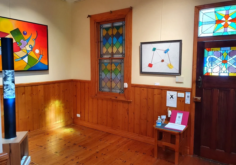 A timber-panelled room inside Matchbox Gallery with leadlight panels in a window and front door and framed artworks on the walls.