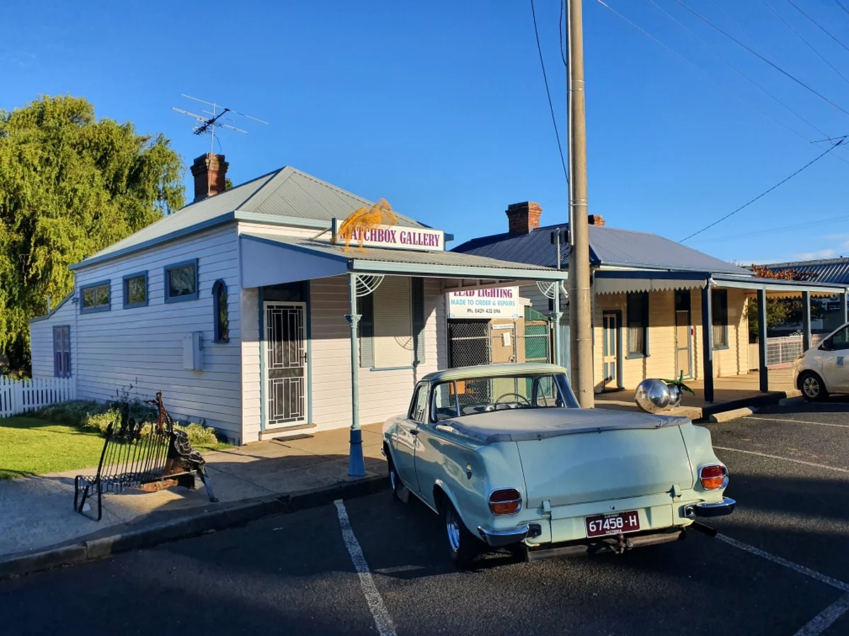 An angled street view of Matchbox Gallery beside neighbouring buildings, with a pale vintage utility parked in the foreground.