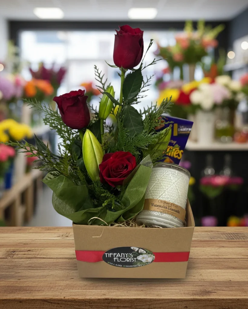 Red roses, lilies, chocolates and a candle arranged in a Tiffany's Florist gift box.