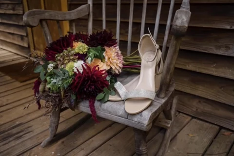 A dark red and blush wedding bouquet with a pale shoe arranged on a wooden chair.