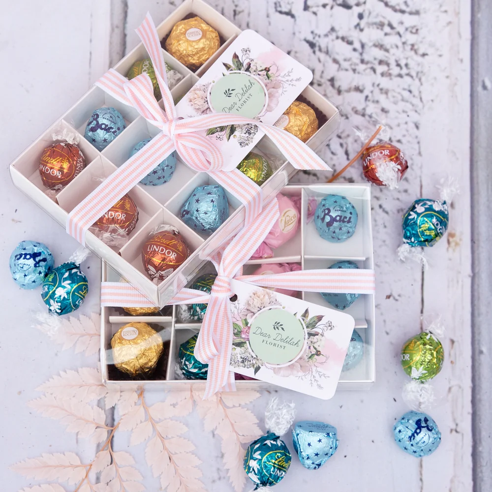Ribboned gift boxes filled with individually wrapped chocolates on a pale timber surface.
