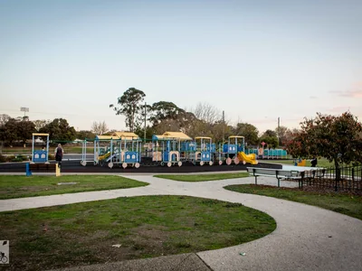 A blue-and-green playground surrounded by lawns and paths at Newman Park.