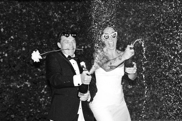 A newlywed couple spray sparkling wine outdoors at night.