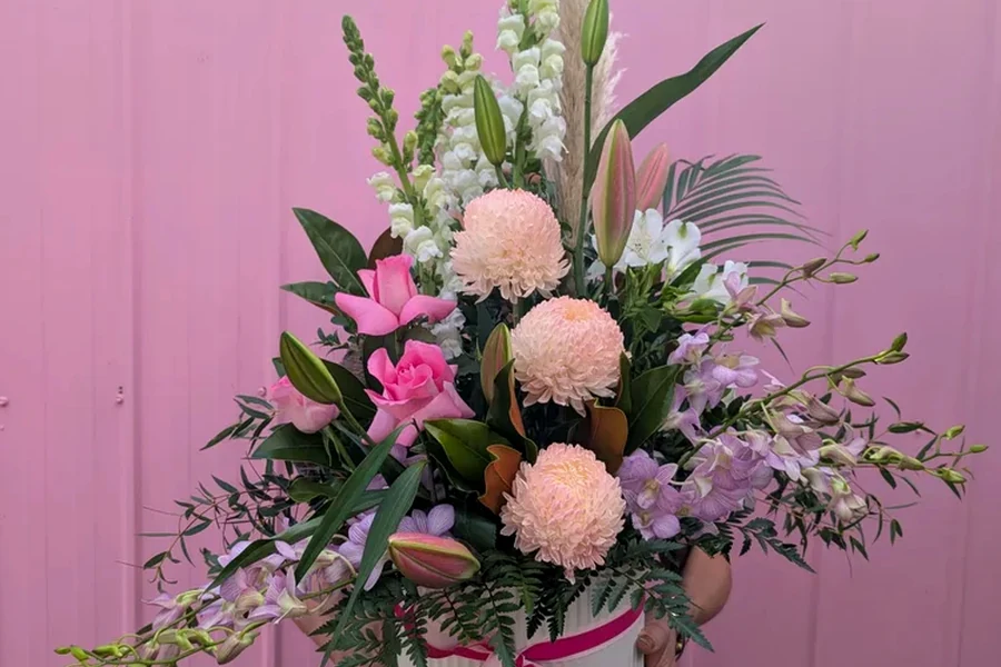 A colourful flower arrangement held in front of a pink wall.