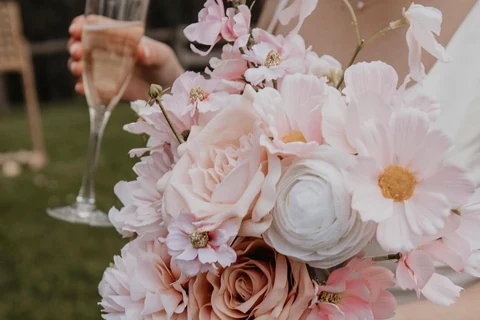 A person in white holds a large pale pink and cream silk bouquet.