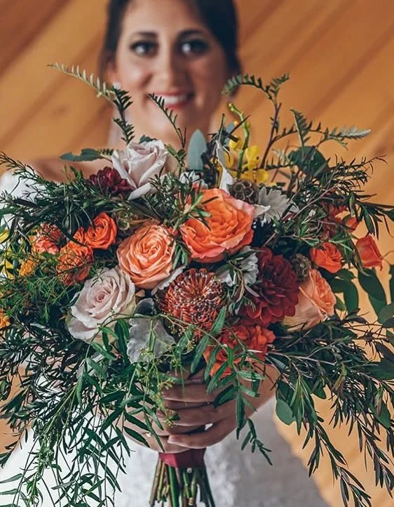 A bride holds a bouquet of orange, burgundy and blush flowers.