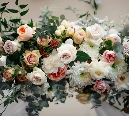 A low, abundant arrangement of cream, blush and muted pink roses and chrysanthemums with eucalyptus foliage.