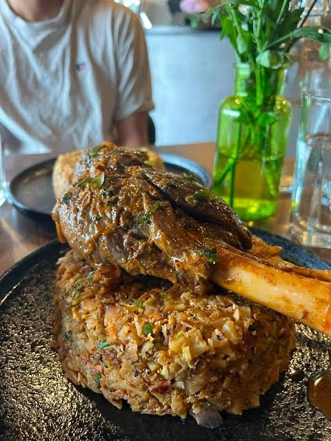 A plated rice dish topped with a large bone-in portion, photographed at a table.