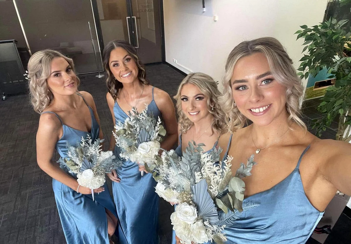 Four people in blue dresses hold coordinated white, silver-green and blue dried bouquets indoors.
