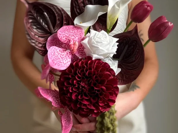 A person holds a sculptural bouquet of deep burgundy, pink and white flowers.