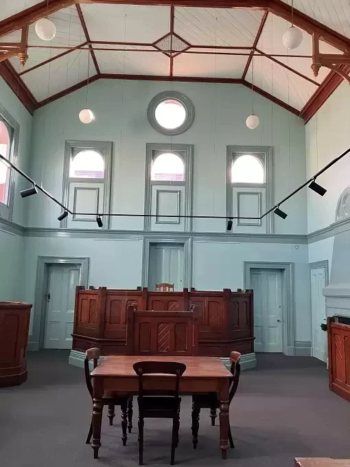 Timber courtroom furniture stands beneath a high pale-green ceiling inside Traralgon Courthouse.