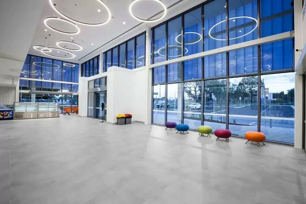 Circular lights and colourful low seats animate the tall glazed foyer of Gippsland Regional Aquatic Centre.
