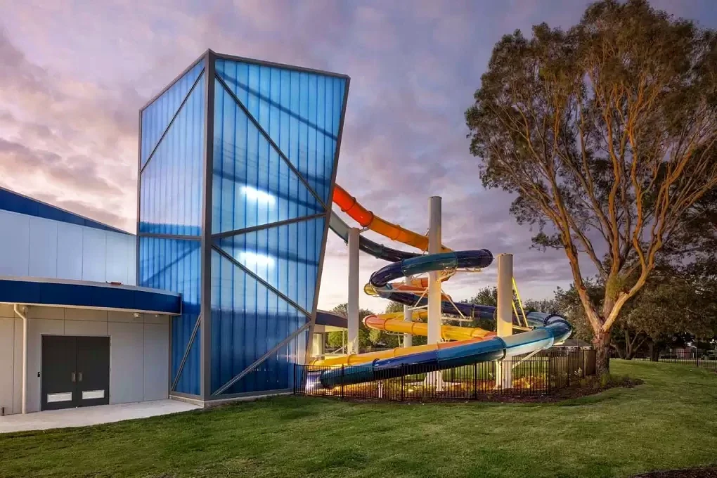 The illuminated blue tower and colourful waterslides of Gippsland Regional Aquatic Centre at dusk.