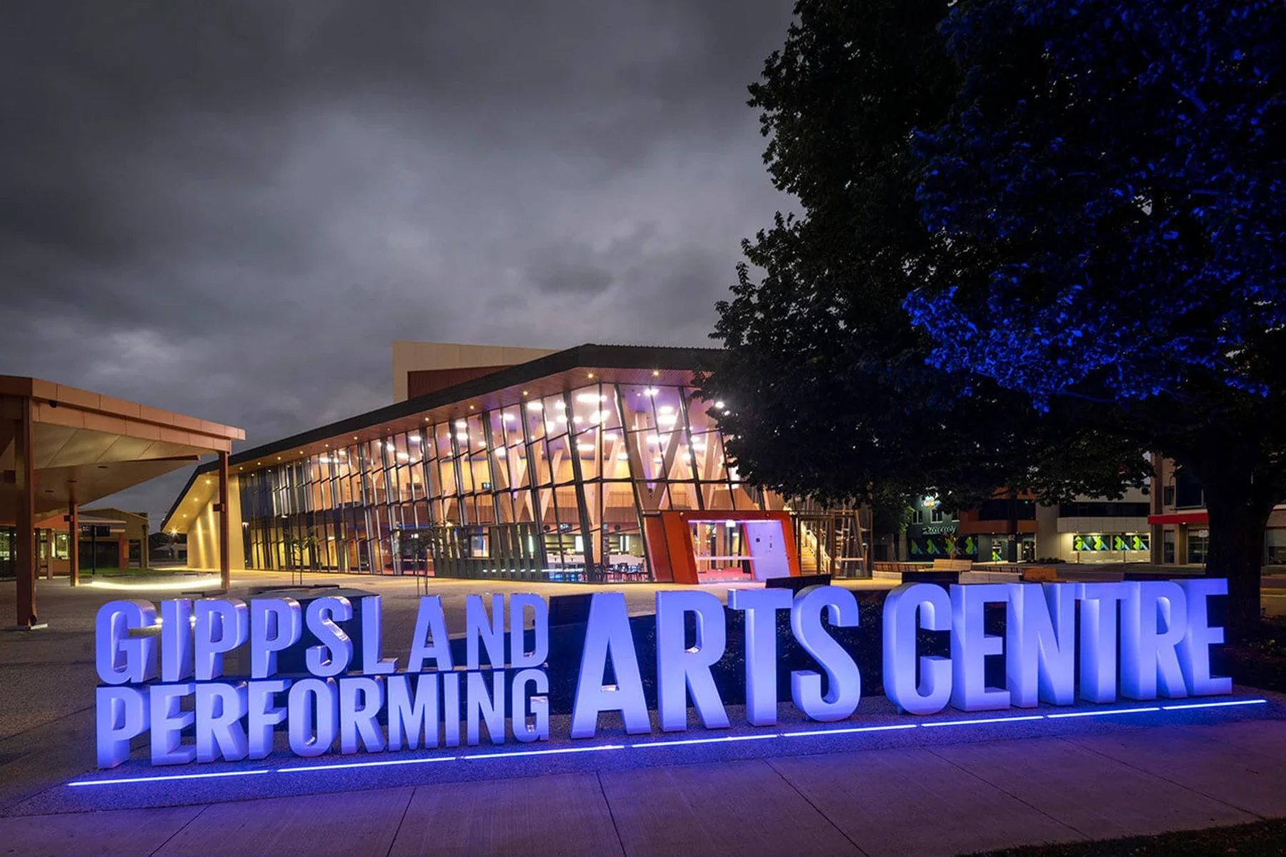 The illuminated Gippsland Performing Arts Centre sign stands before its glass foyer at night.