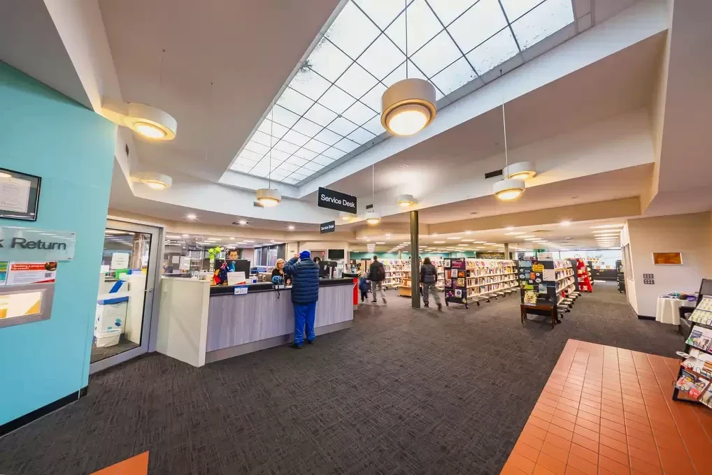 Visitors use the service desk and browse mobile bookshelves beneath Traralgon Library's skylight.