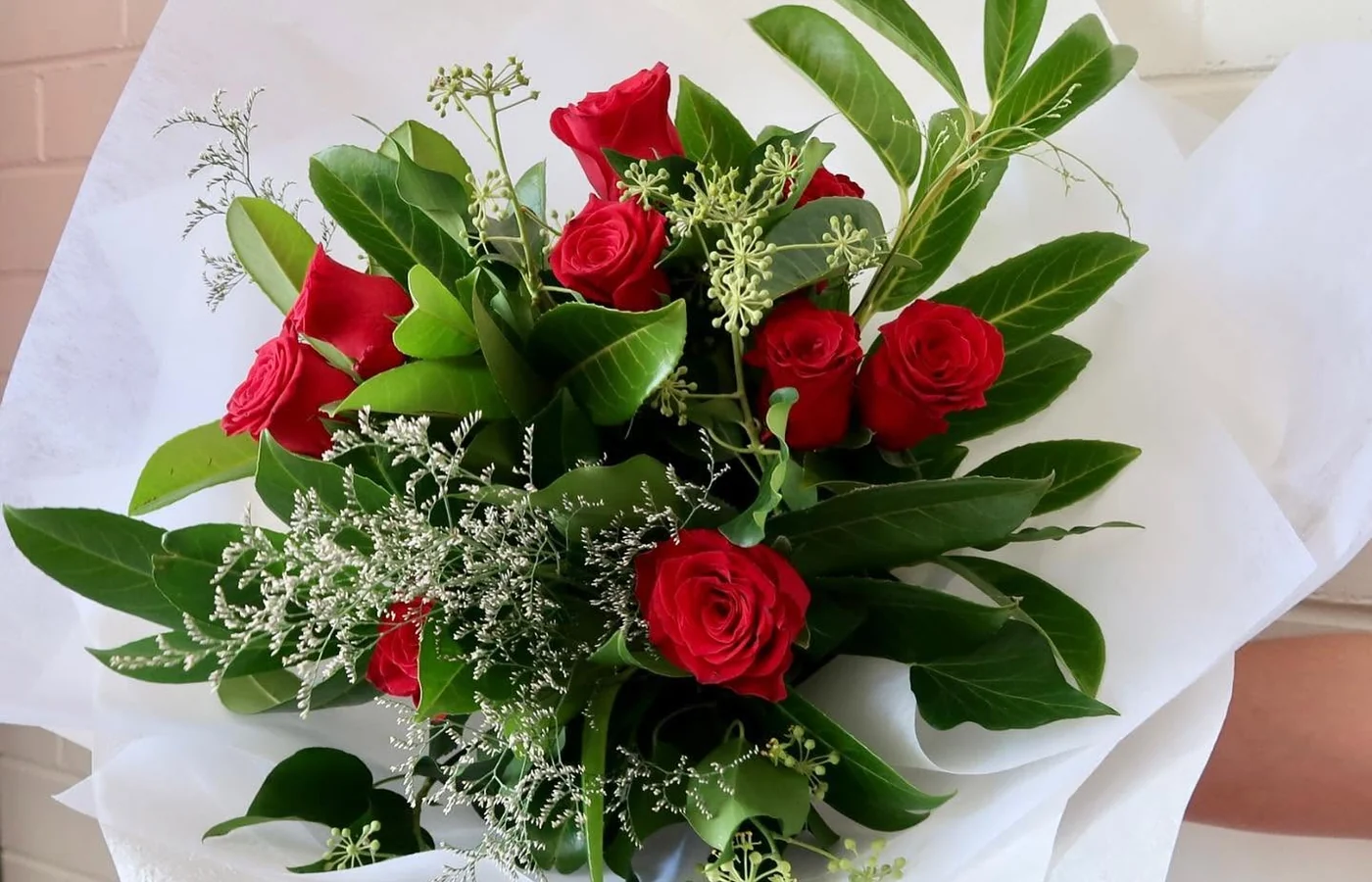 A bouquet of red roses and green foliage wrapped in white paper.