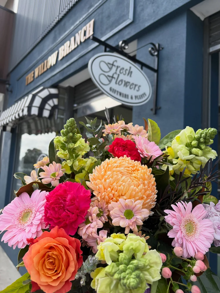 A colourful bouquet of roses, chrysanthemums, gerberas and snapdragons outside The Willow Branch storefront.