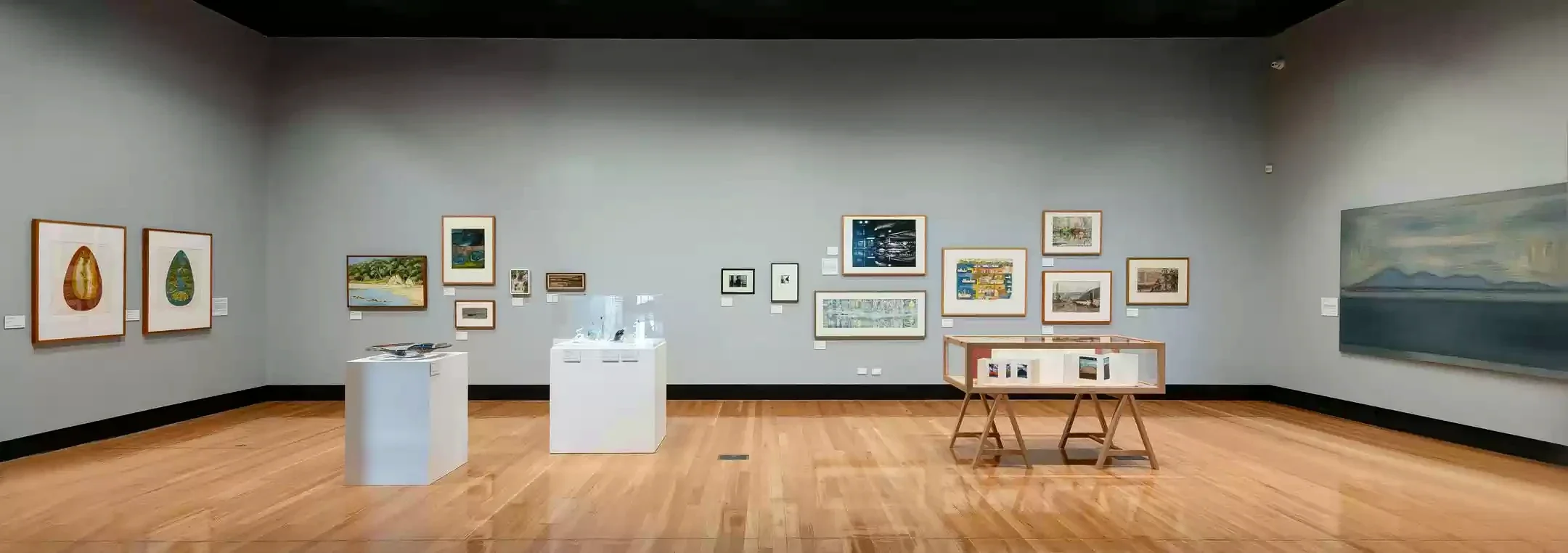 A wide Latrobe Regional Gallery exhibition room with framed works and display cases.