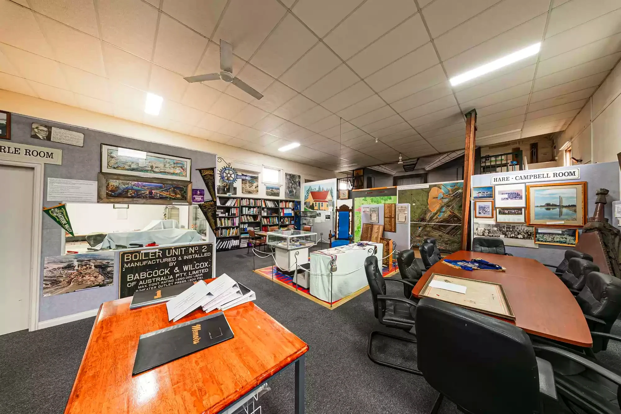 Maps, industrial objects, photographs and labelled rooms fill a Morwell Historical Society collection space.