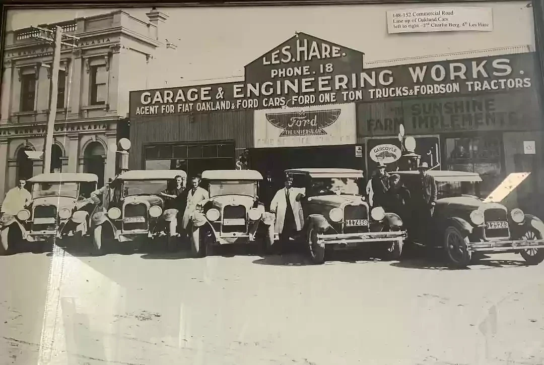 A historic display photograph shows people and early cars outside Les Hare's garage and engineering works in Morwell.