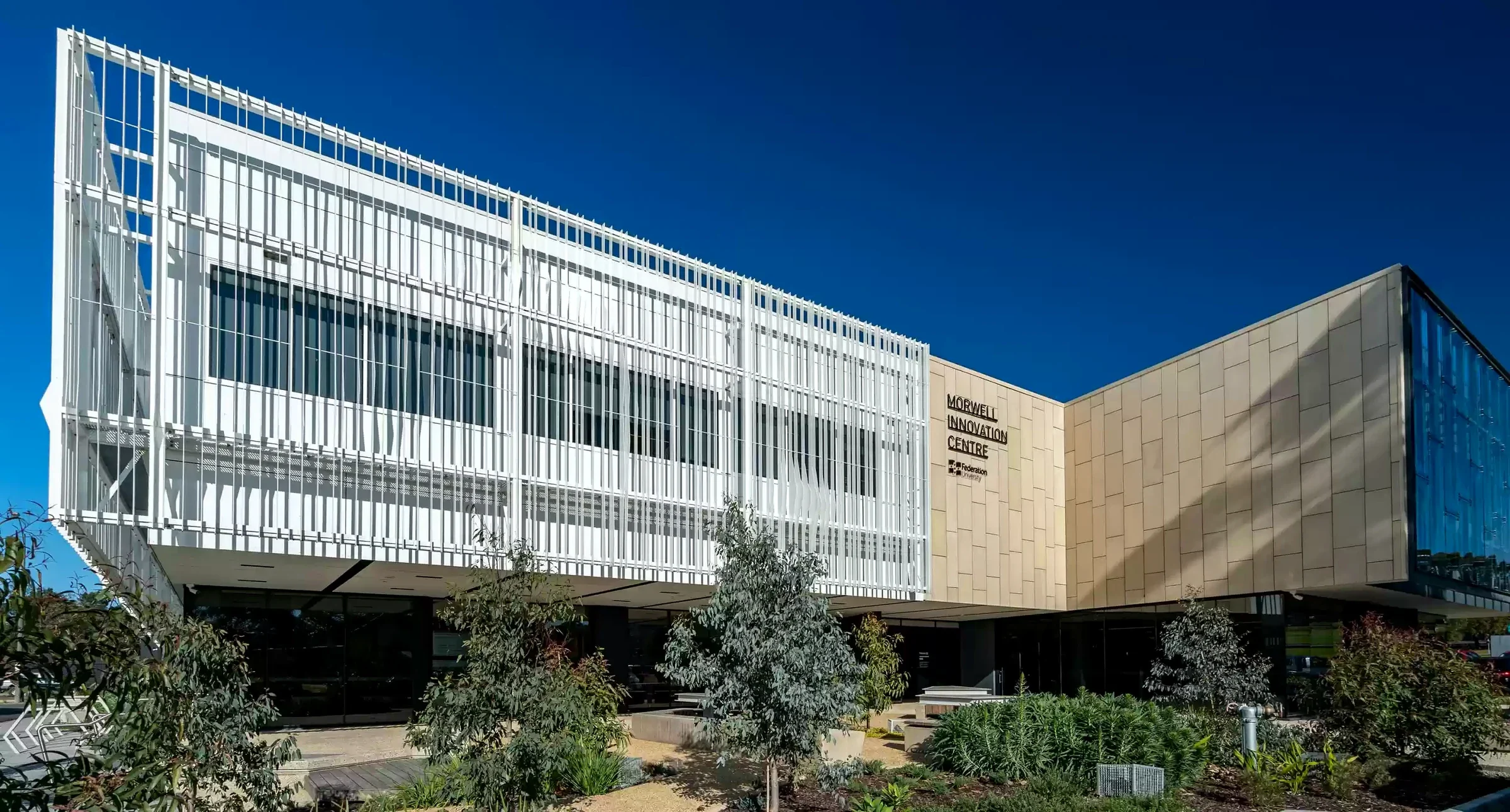 The white screens and bronze-toned wing of Morwell Innovation Centre beneath a deep blue sky.
