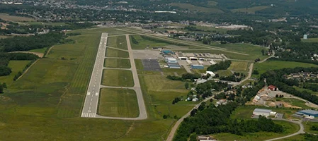 Aerial view of a long airport runway with buildings and surrounding green land.