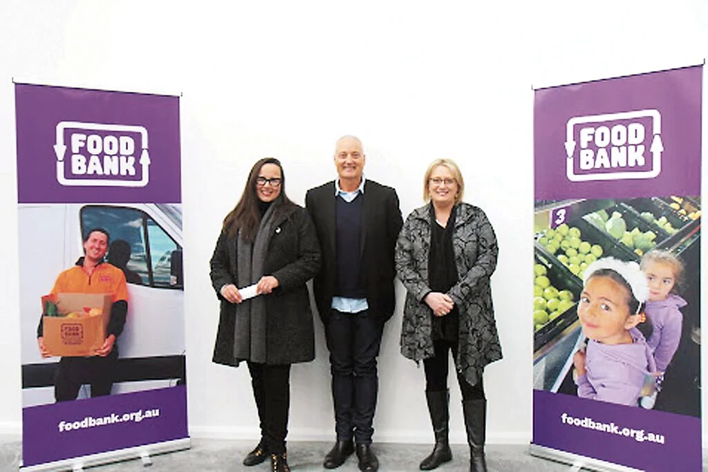 Three adults standing between two Foodbank display banners.