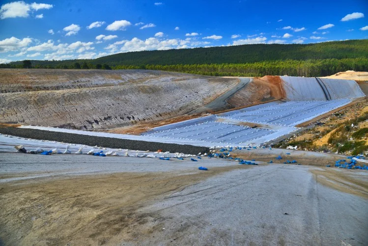 A broad view across an excavated landfill cell with liner installation in progress.