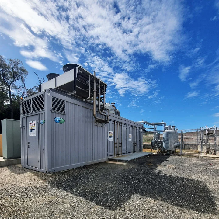 Containerised landfill-gas equipment with pipes and cooling fans beneath a blue sky.