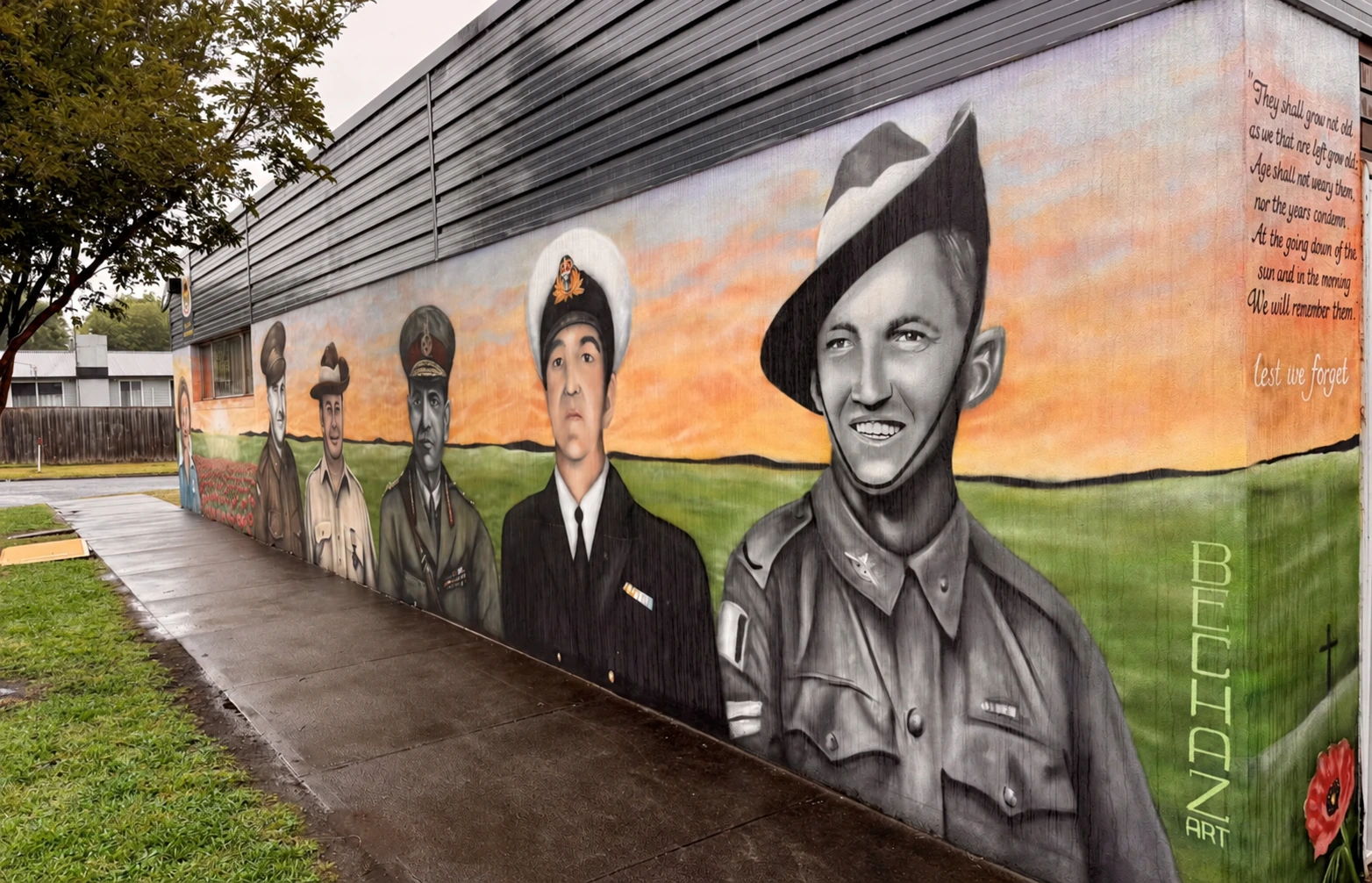 Newborough community mural honouring service people beside a rain-darkened footpath and green lawn
